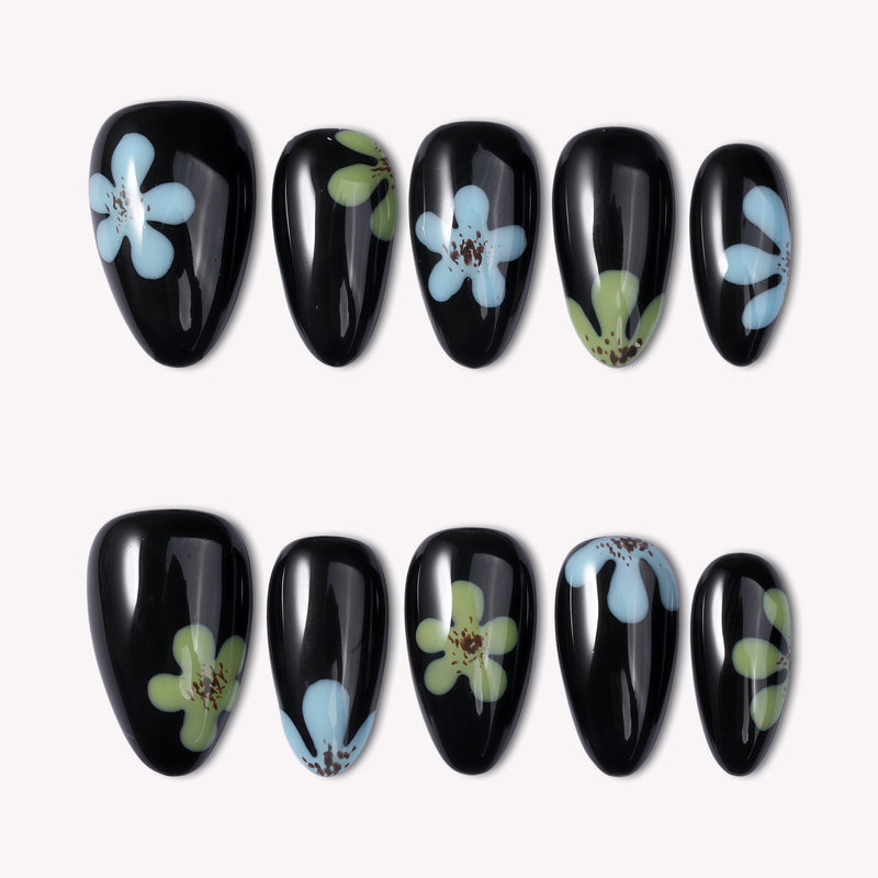 Glossy black press-on nails with blue and green flower designs arranged in two rows on a white background.