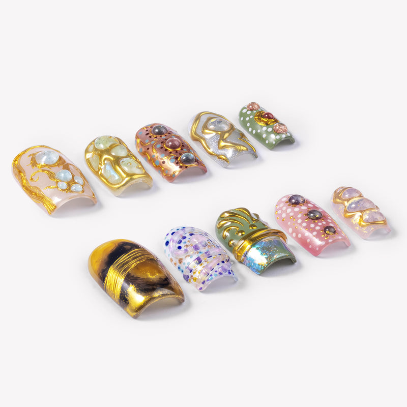 Angled flat lay of Golden Muse gold, opal, pink and green statement press-on nails with raised jeweled details