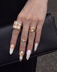 Hand close-up wearing Golden Shell white and gold seashell nails with gold rings on a black clutch