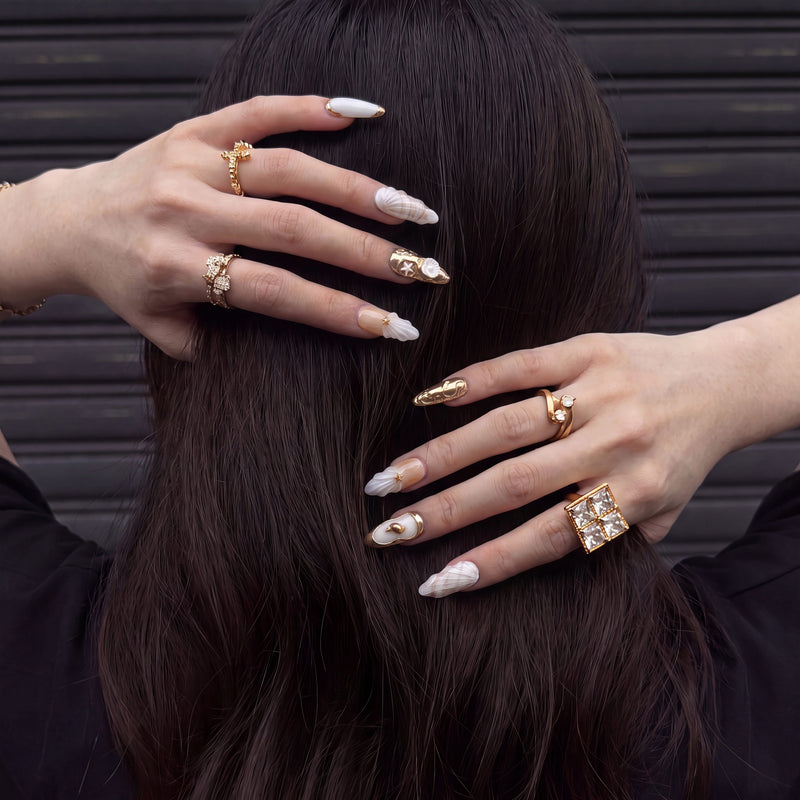 Model wearing Golden Shell white and gold seashell press-on nails with gold rings against dark hair