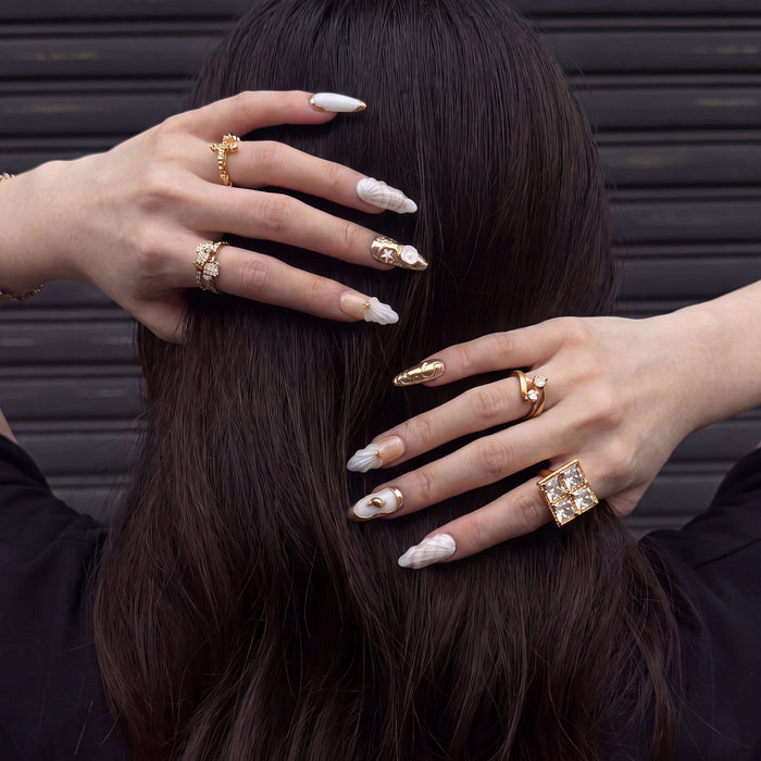 Model wearing Golden Shell white and gold seashell press-on nails with gold rings against dark hair