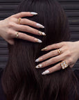 Model wearing Golden Shell white and gold seashell press-on nails with gold rings against dark hair