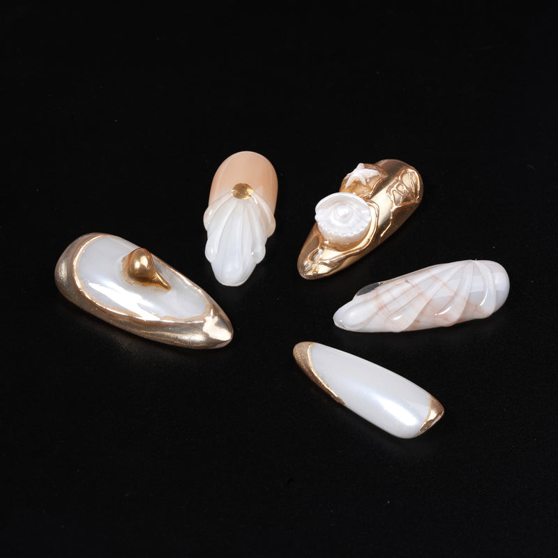Detail flat lay of Golden Shell white and gold press-on nails with sculpted seashell and pearl accents
