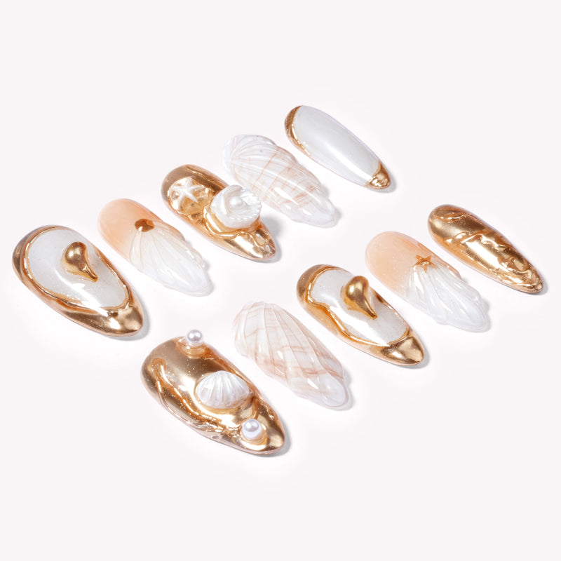 Angled flat lay of Golden Shell white and gold seashell nails with pearls and sculpted shell details