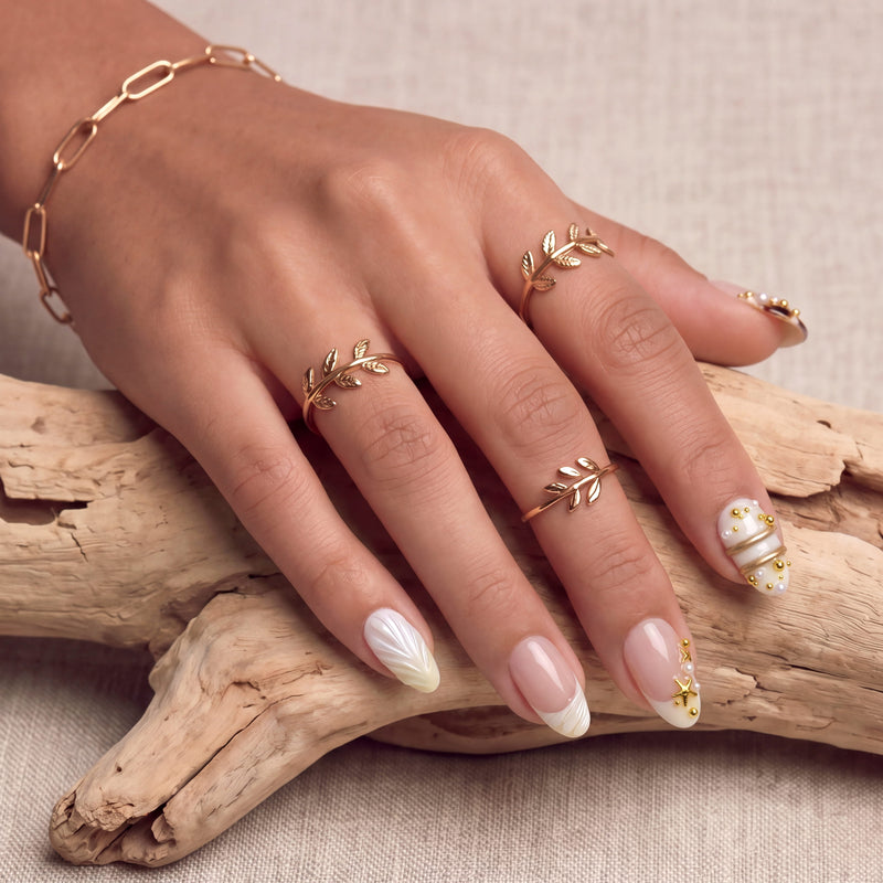 Hand model wearing Golden Shore Ritual handmade press-on nails with ivory and gold accents on a rustic stone background.