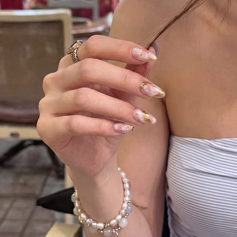 Close-up hand model wearing Golden Veil peach marble press-on nails with raised gold details and pearl accents