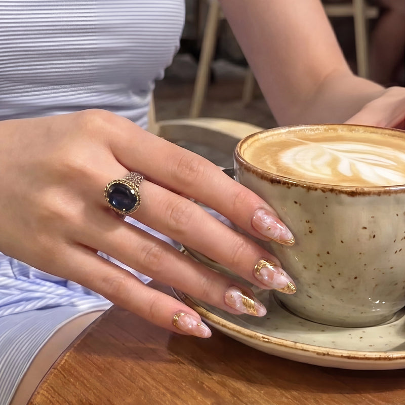 Hand model holding a latte while wearing Golden Veil peach marble press-on nails with gold accents and pearls