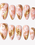 Golden Veil peach marble press-on nails with sculpted gold foil accents and pearl embellishments in a flat lay
