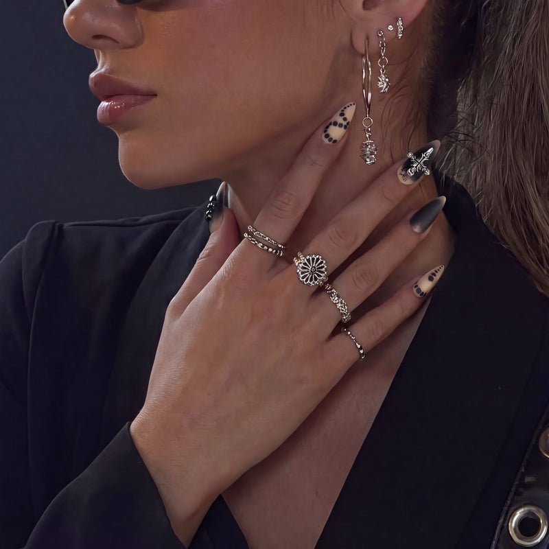 Close-up hand model in a black blazer wearing Gothic Elegance press-on nails with nude dot patterns, matte black tips, silver cross detail, and rings