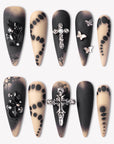 Gothic Elegance press-on nails with matte black and nude designs, silver cross charms, black rhinestones, lace effects, and butterfly accents