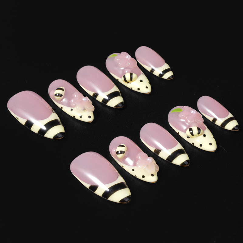 Pink press-on nails with bee-inspired stripes, polka dots, and floral accents