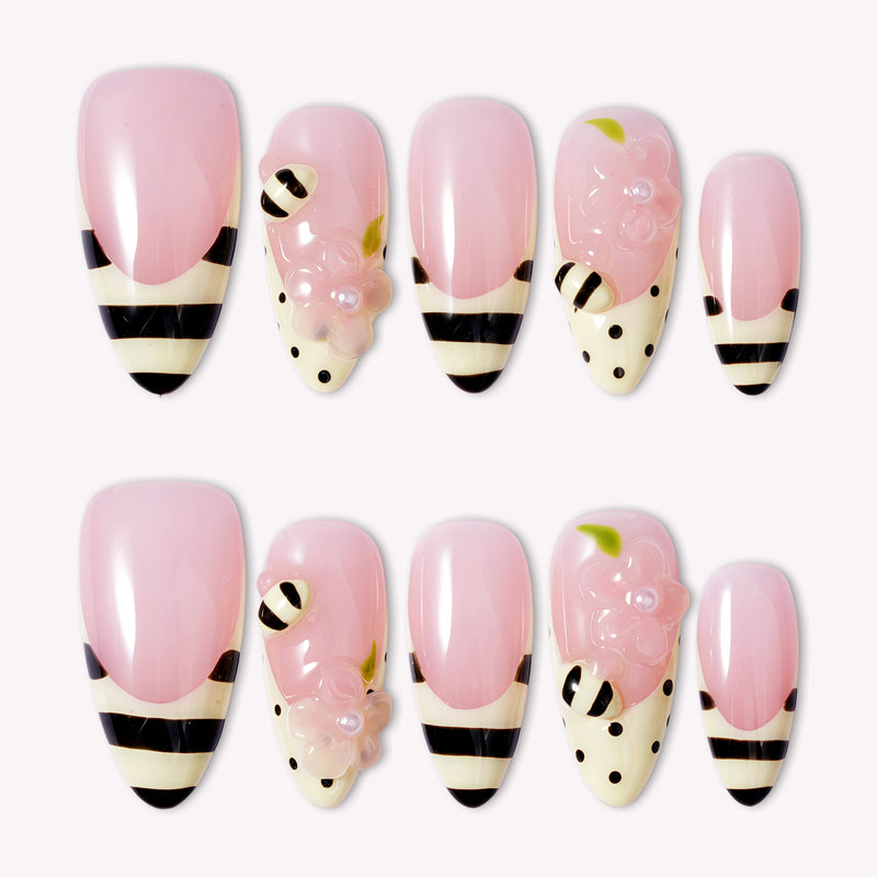 Pink press-on nails with bee-inspired stripes, polka dots, and floral accents arranged in a flat lay