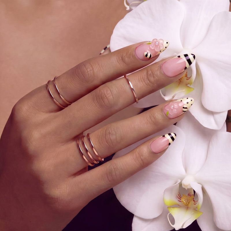 Pink press-on nails with bee-inspired stripes, polka dots, and floral accents arranged in a set layout