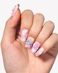 Hand model wearing Impressionist Pointe press-on nails with pink yellow gradients, 3D flowers, pearls, and bow accents