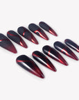 Angled flat lay of Inferno Veins stiletto press-on nails with metallic red gradients, matte black panels, glossy black sections, and vein-like curves