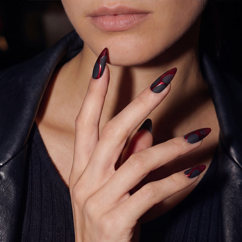 Hand model in a black leather jacket wearing Inferno Veins stiletto press-on nails with matte black sections and metallic red vein designs