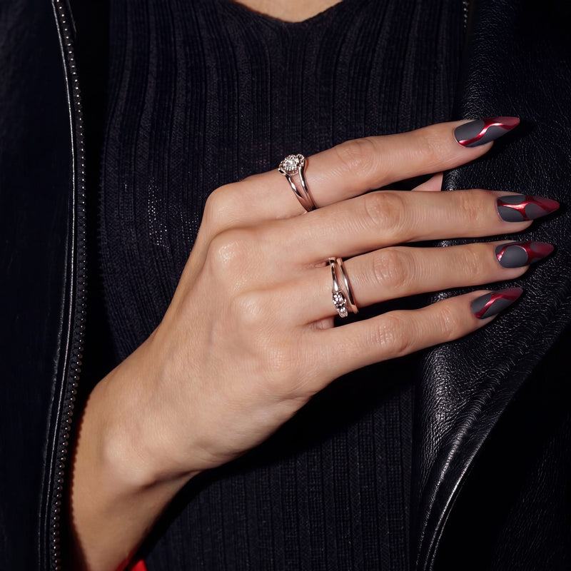 Hand model on a black outfit wearing Inferno Veins stiletto press-on nails with matte black panels, metallic red vein accents, and silver rings