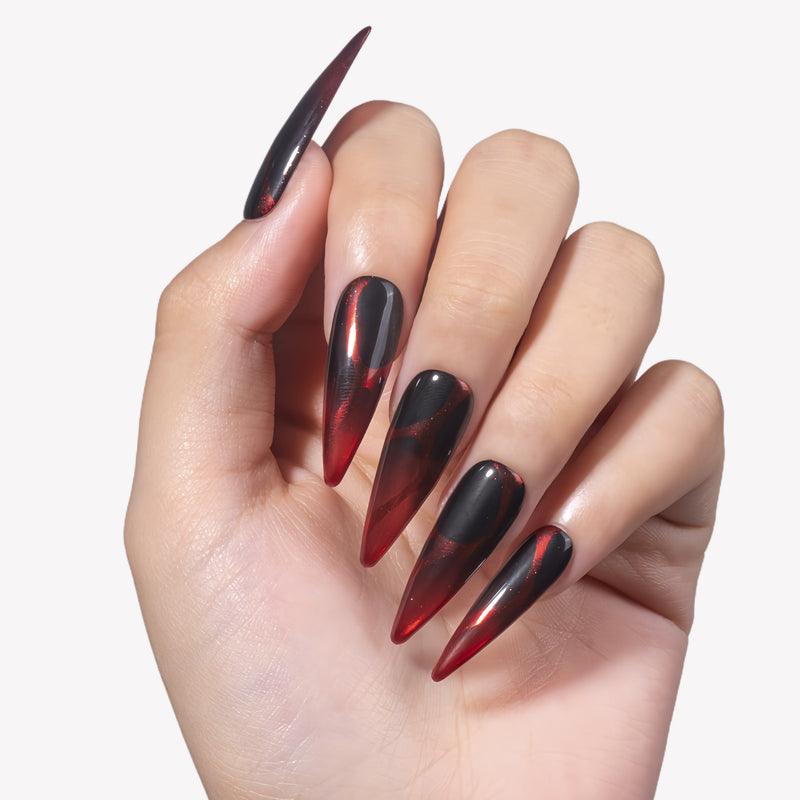 White background hand model wearing Inferno Veins stiletto press-on nails with translucent red tips, black curved panels, and glossy finish