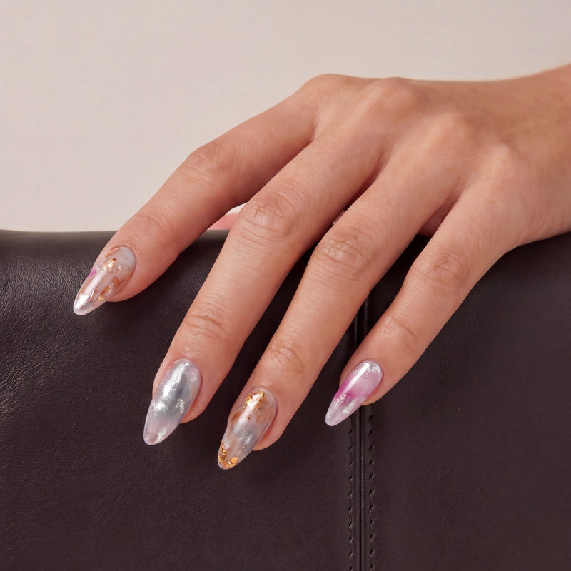 Close-up of a hand model wearing iridescent pearl press-on nails in silver, blush pink, and gold foil
