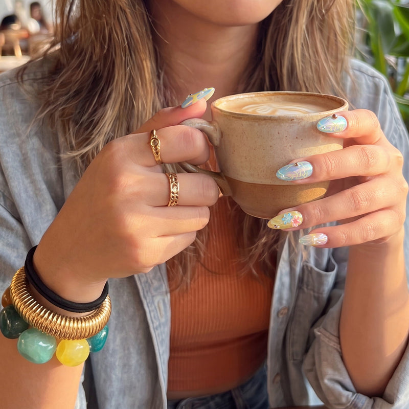 Cafe lifestyle view of a model holding a coffee cup while wearing Iridescent Petals pastel floral press-on nails