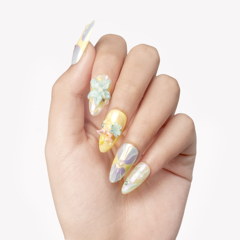 Hand close-up wearing Iridescent Petals pastel press-on nails with raised blue and pink flowers, pearls and gems