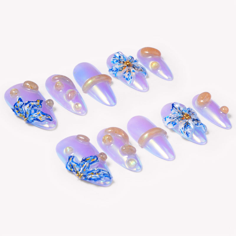 Angled flat lay of Iris Bloom iridescent purple nails with blue sculpted flowers and golden pearl accents