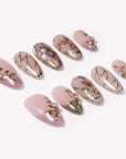 Flat lay of blush pink floral press-on nails with gold stained-glass linework and pearl accents.
