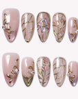 Flat lay of blush pink and gold floral press-on nails with stained-glass line art and tiny rhinestone accents.