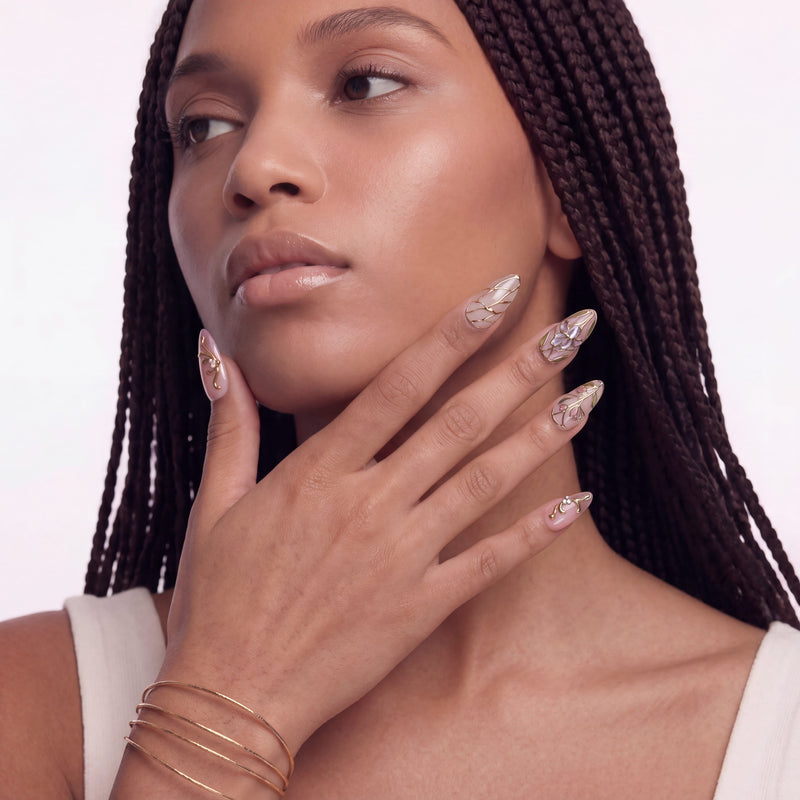 Portrait of a hand model wearing gold floral stained-glass press-on nails with a white background.