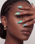 Hand model wearing turquoise almond press-on nails with yellow and pink floral accents