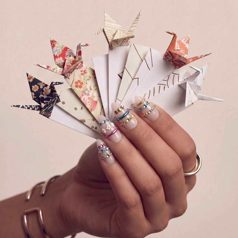 Jewel Band handmade press-on nails on a hand model holding folded paper fans with multicolor gemstone bands