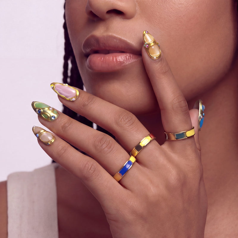Face hand model wearing Jewel Mosaic press-on nails with pastel panels, raised gold outlines, and colorful rhinestones