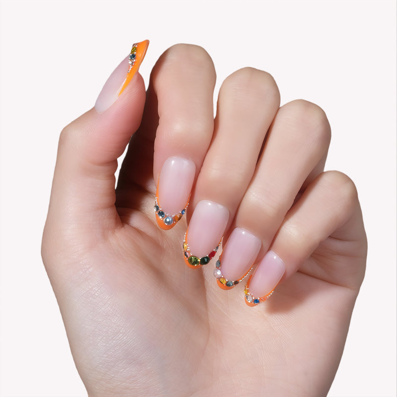 Close-up of a hand model wearing Jewel Sunset press-on nails with ruby red tips and multicolor gem accents