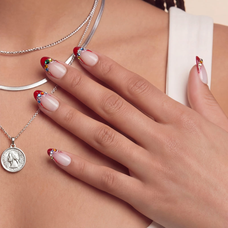 Lifestyle portrait of a hand model wearing Jewel Sunset press-on nails with ruby red tips and multicolor gem accents