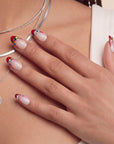 Lifestyle portrait of a hand model wearing Jewel Sunset press-on nails with ruby red tips and multicolor gem accents