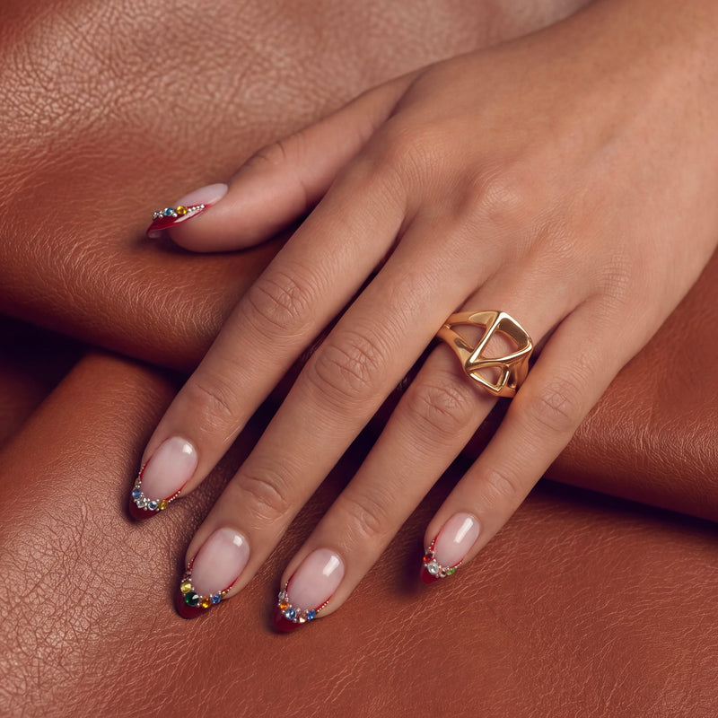 Lifestyle portrait of a hand model wearing Jewel Sunset press-on nails with ruby red tips and multicolor gem accents