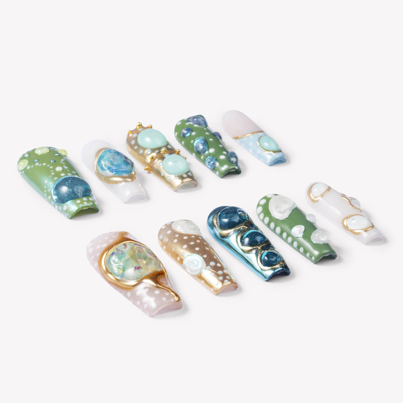 Angled flat lay of Jungle Relic green, blue, ivory and gold press-on nails with dimensional gem accents