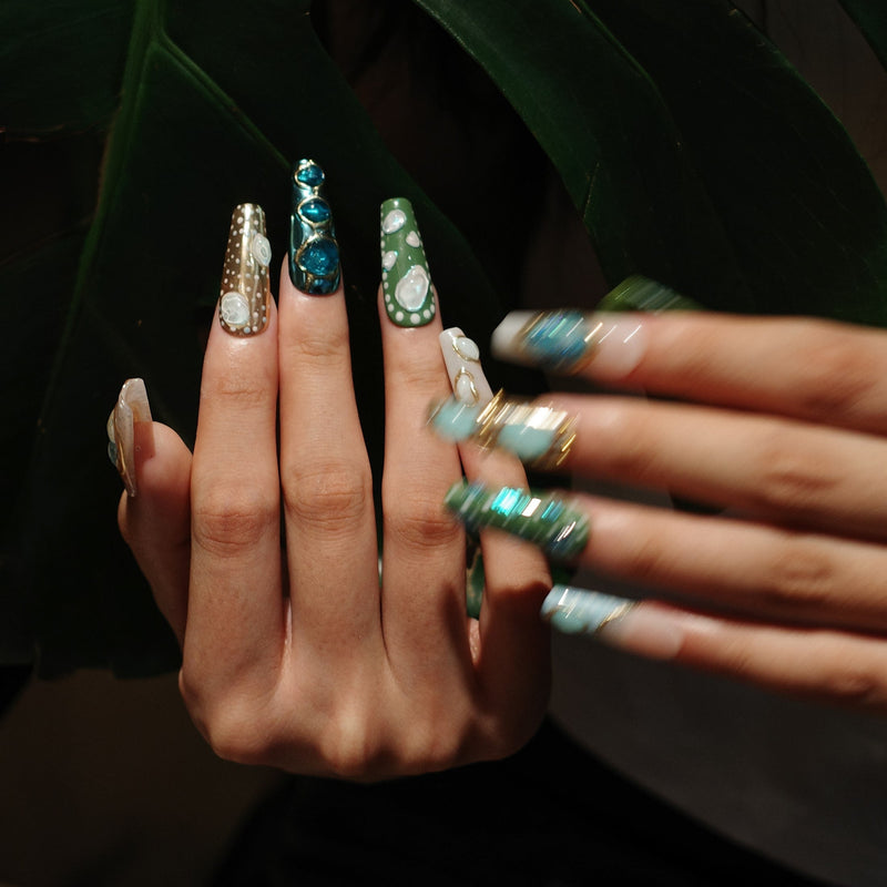 Jungle Relic long green, turquoise and brown press-on nails with raised gems and white relic details against tropical leaves