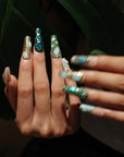 Jungle Relic long green, turquoise and brown press-on nails with raised gems and white relic details against tropical leaves