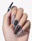Close-up hand model wearing Lace & Pearls press-on nails with black matte finish, white lace pattern tips, and pearl accents