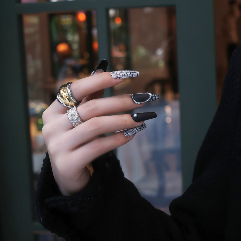 Hand model wearing Lace & Pearls press-on nails with black matte tips, white lace pattern accents, pearl trim, and statement rings