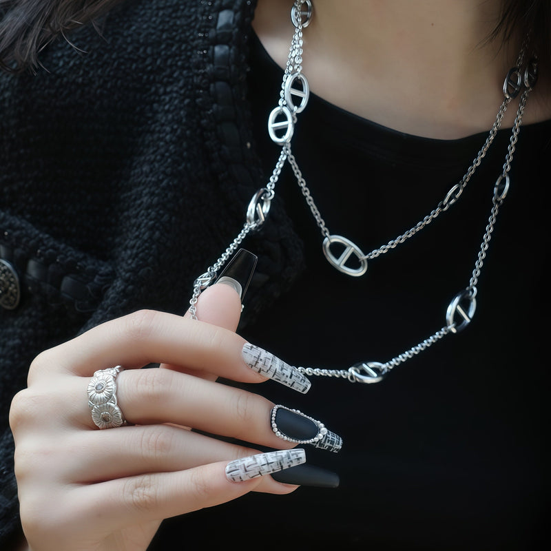 Lifestyle close-up of Lace & Pearls press-on nails with black matte tips, pearl trim, and white lace accents beside silver chain jewelry