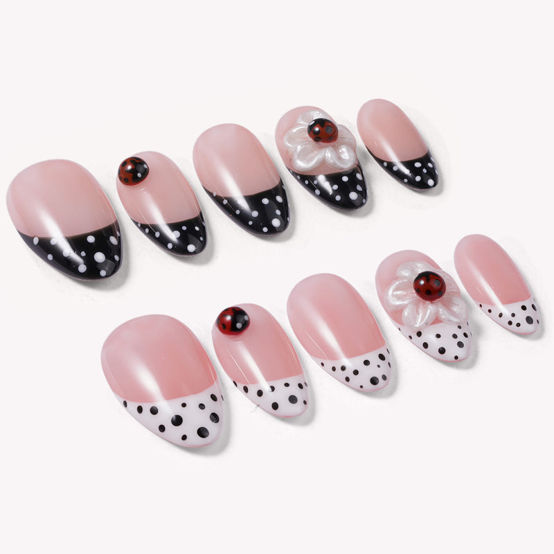 Angled flat lay of Ladybug Garden press-on nails with pink bases, black and white polka dot French tips, red ladybugs, and white flower charms