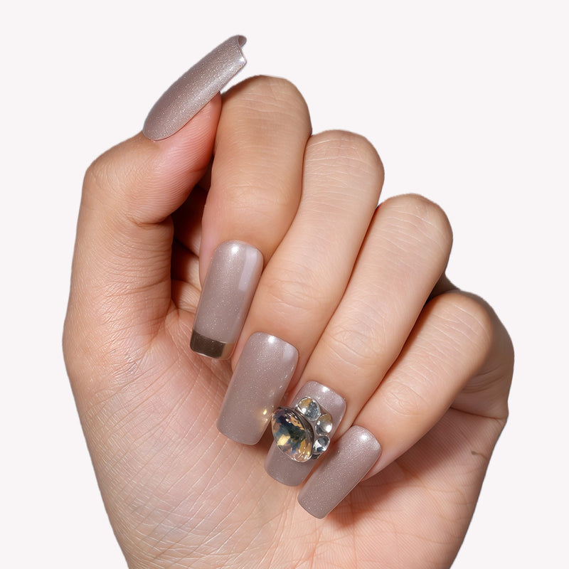 Hand model wearing metallic taupe press-on nails with a gemstone accent