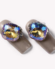Close-up of champagne metallic press-on nails with oversized iridescent gemstone accents