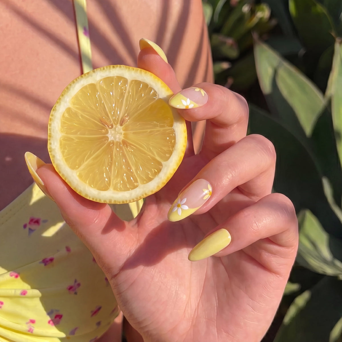 Model holding a lemon while wearing Lemon Bloom yellow and white floral press-on nails in sunlight