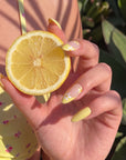 Model holding a lemon while wearing Lemon Bloom yellow and white floral press-on nails in sunlight