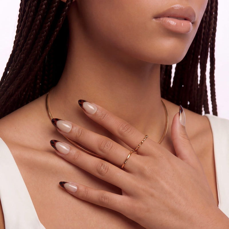 Hand model wearing Leopard French press-on nails with glossy nude bases and deep brown animal print French tips styled with gold rings