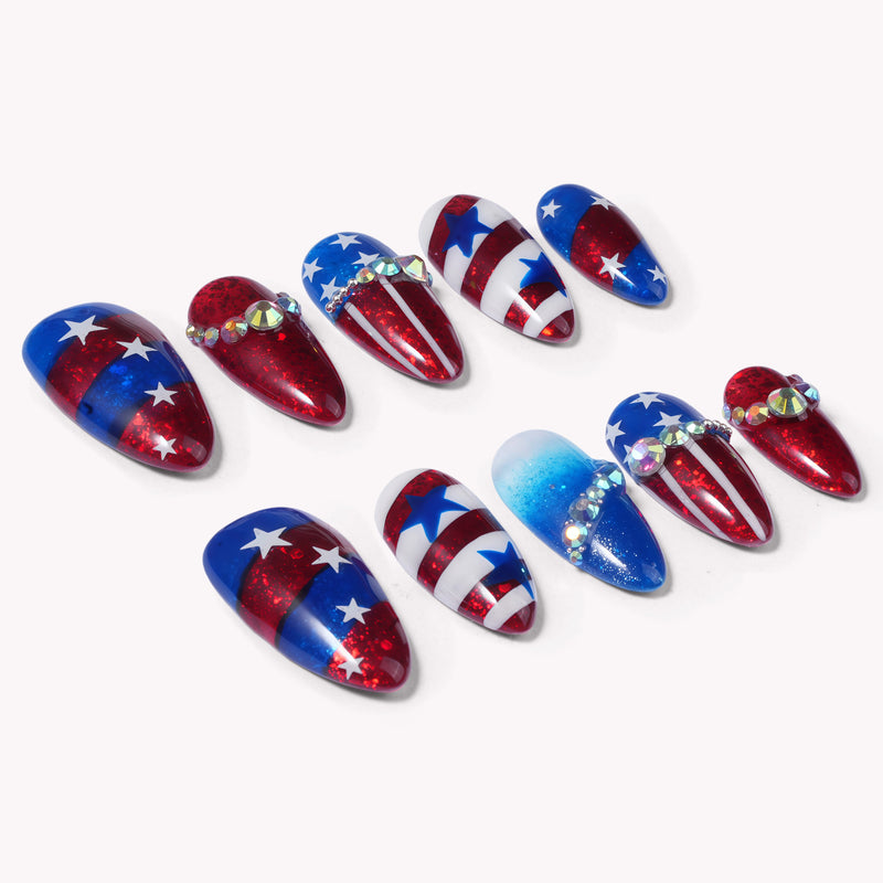 Flat lay of red, white, and blue patriotic press-on nails with glitter, stars, stripes, and rhinestone accents on a white background.