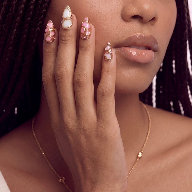 Model wearing Liquid Gold pink and white sculpted press-on nails with raised rose gold details near her face